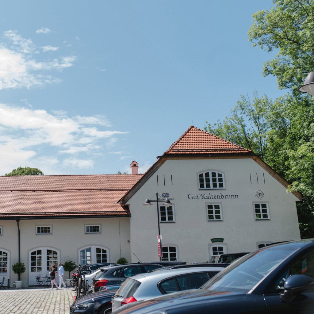 Charmantes Gebäude der Hochzeitslocation Gut Kallenbrunn in München mit Parkplätzen und grüner Umgebung, ideal für unvergessliche Hochzeiten.
